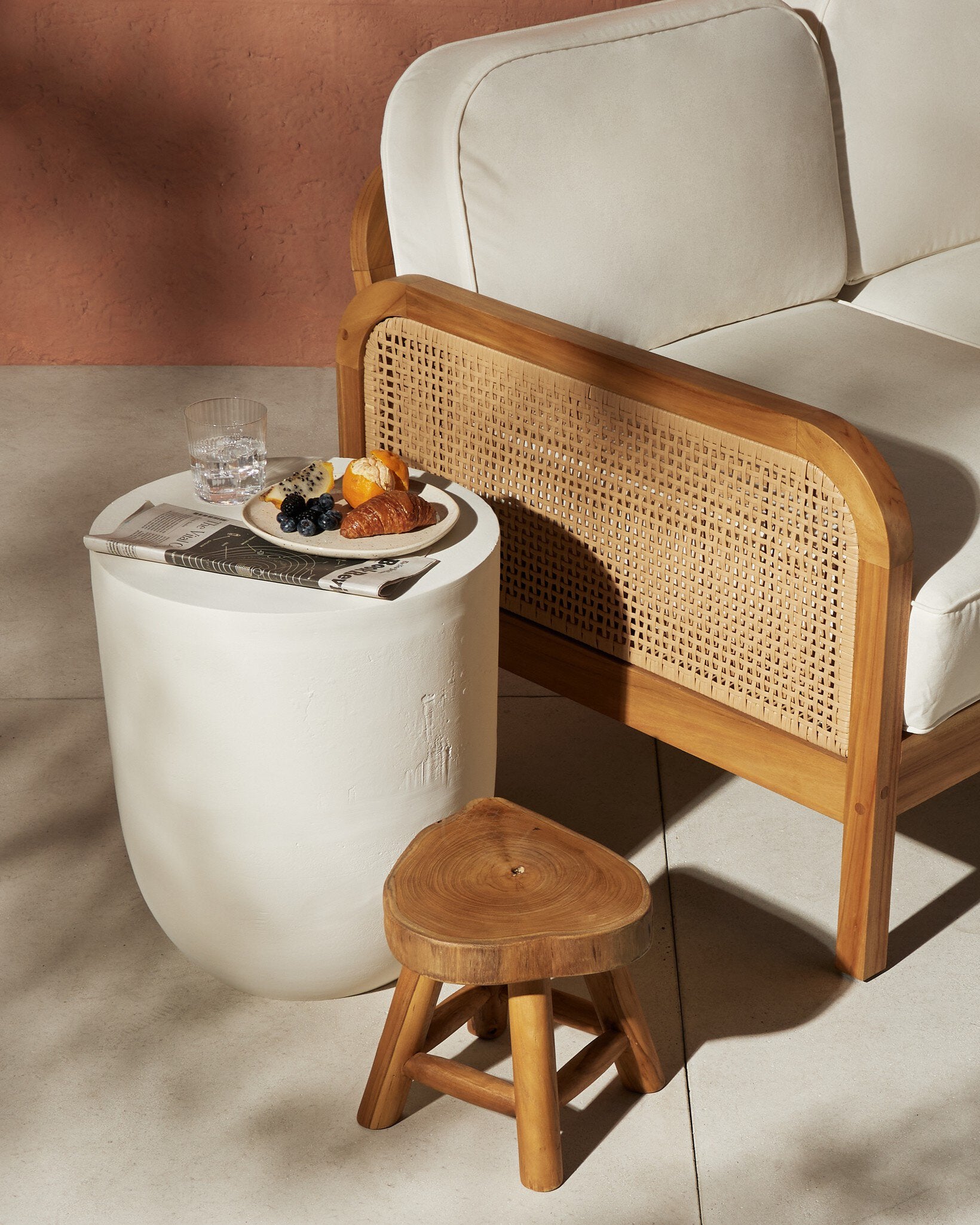 White side table with a plate of food next to a wooden armchair with wicker backrest.