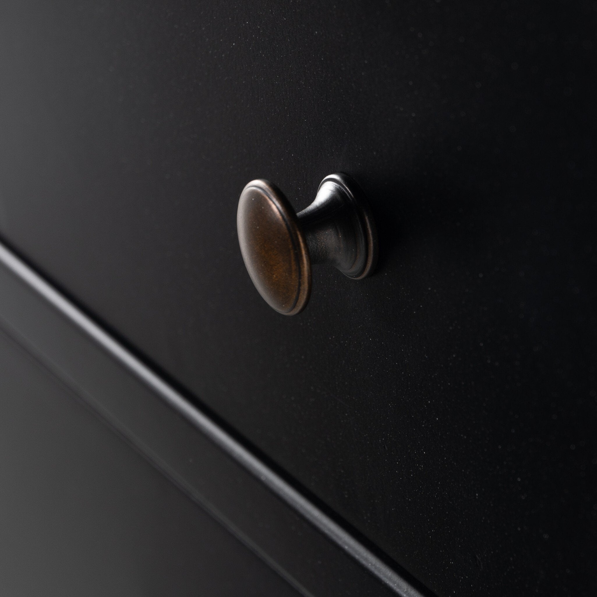 A close up of a black dresser with three drawers and metallic knobs on a white background.