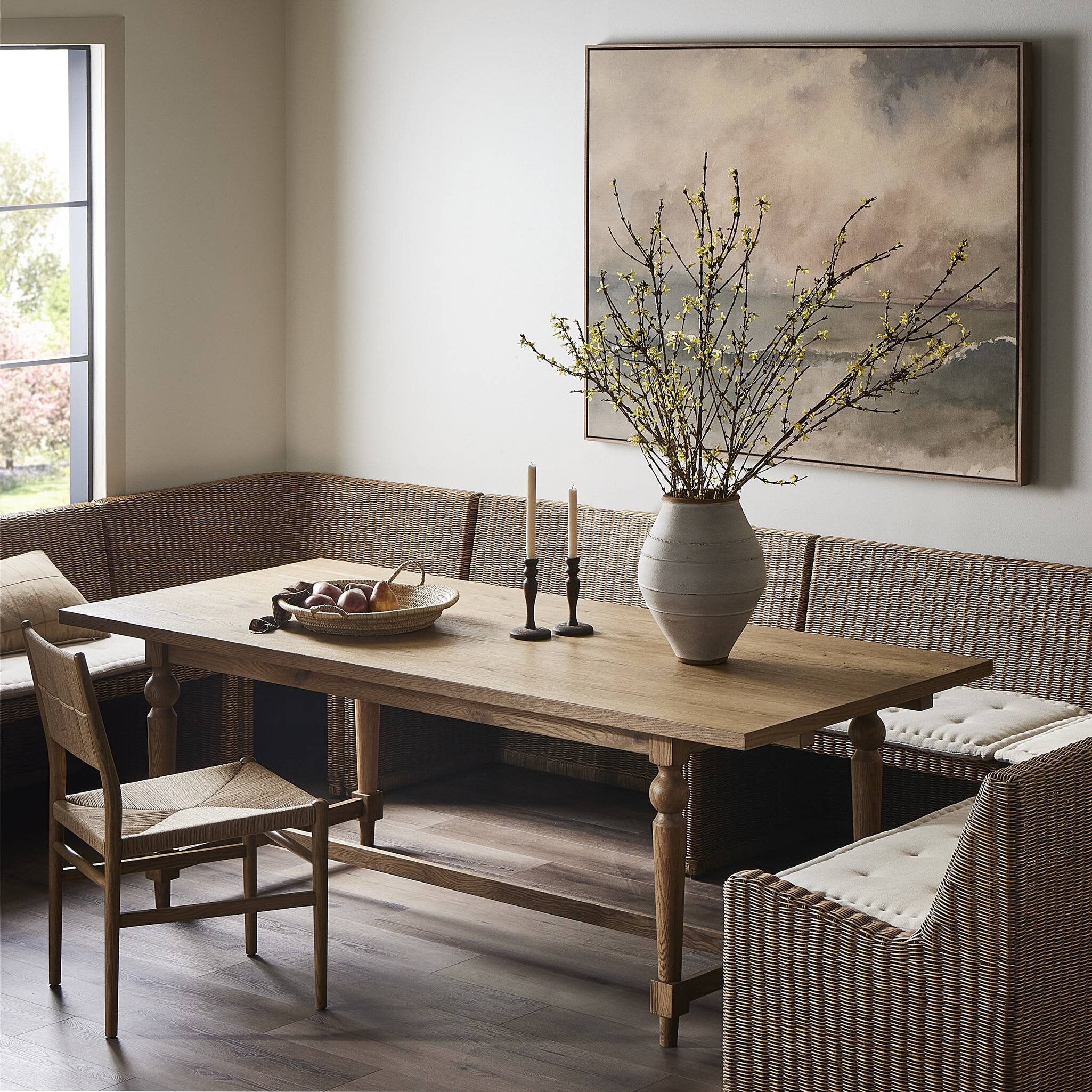 Dining room with wooden table, chairs, and a vase with branches on the wall.