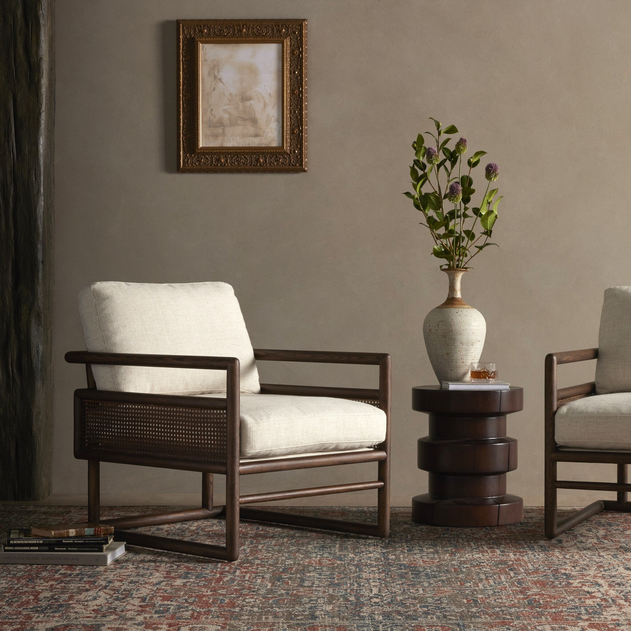 Two armchairs in a room with a framed picture and a vase on a small table.