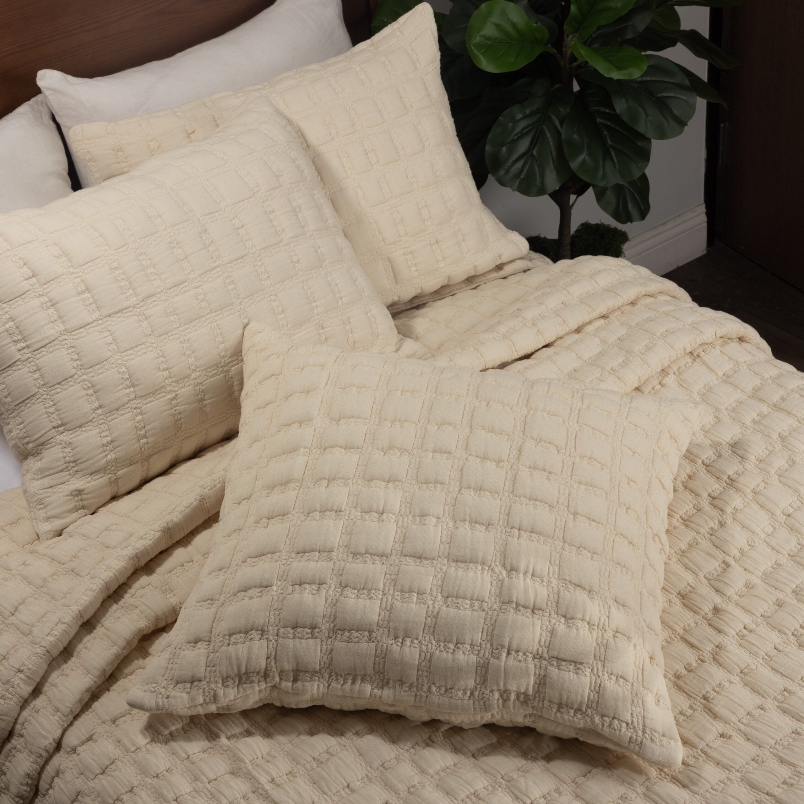 Cream quilt and matching shams layered on a bed, highlighting the plush grid texture and soft cotton finish.