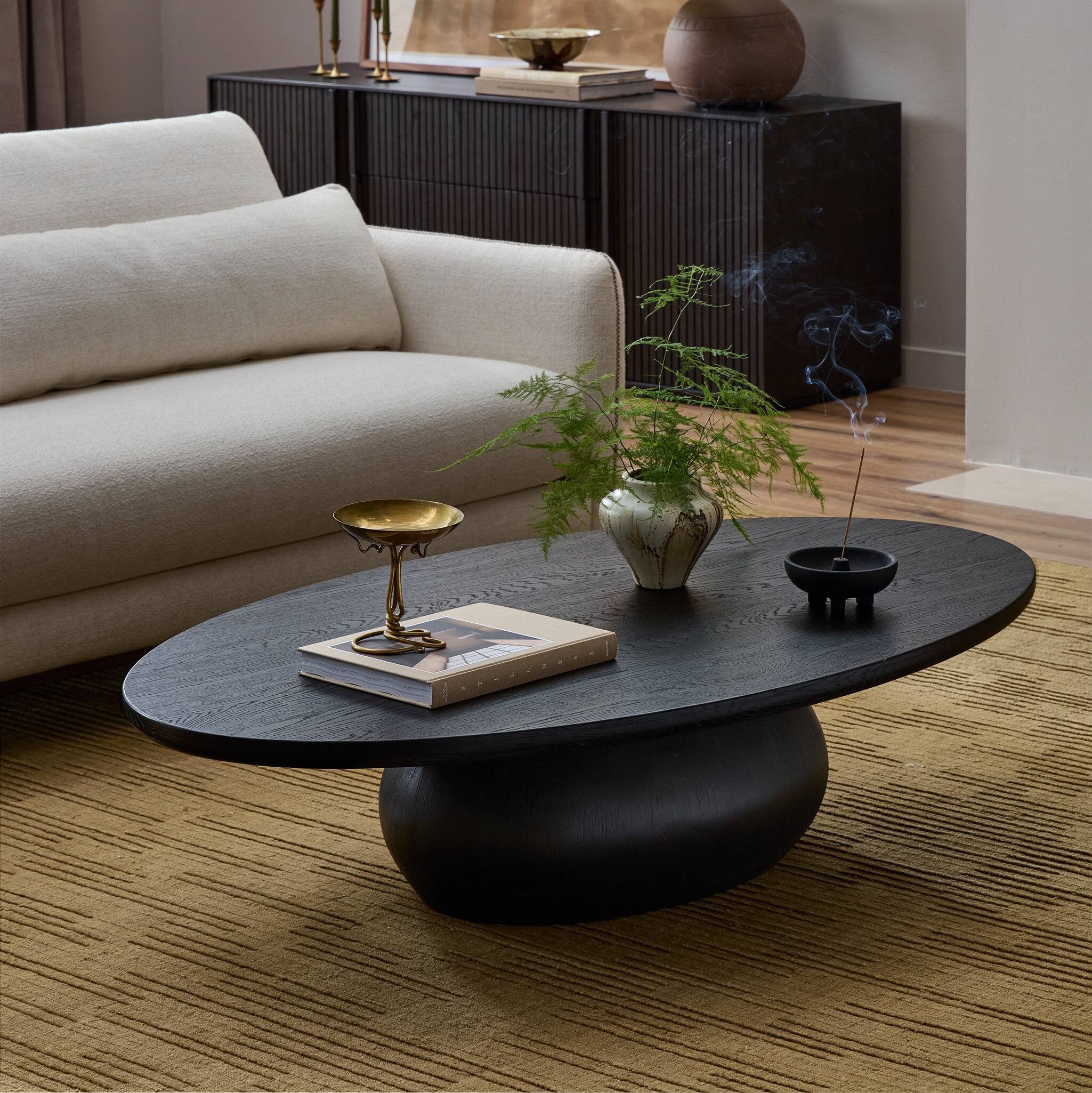 Modern living room with a black coffee table, beige sofa, and decorative items.