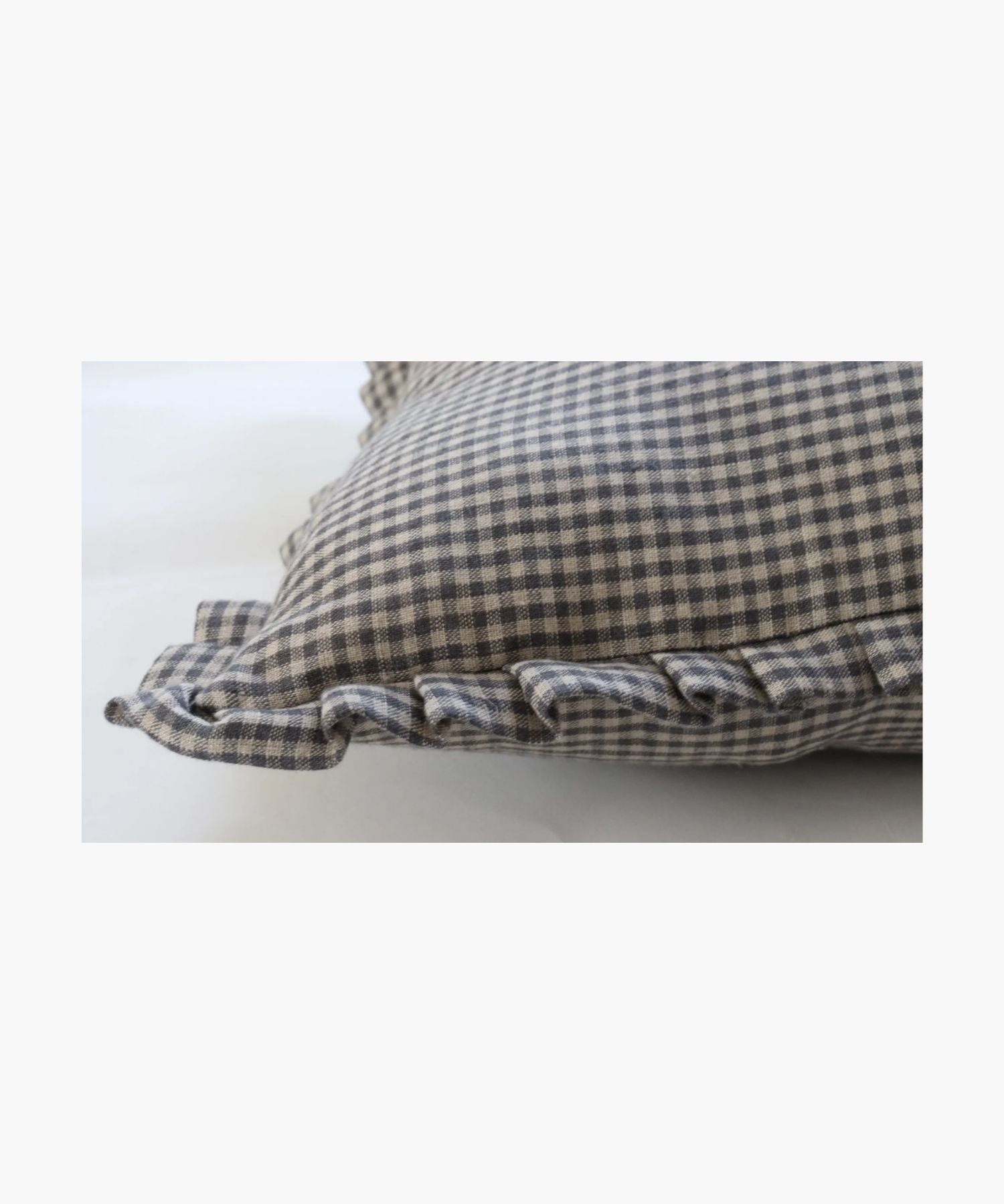 A detailed picture of a pillow highlightings its black and white gingham pattern and ruffled edges, conveying a classic and cozy feel, set against a plain background.