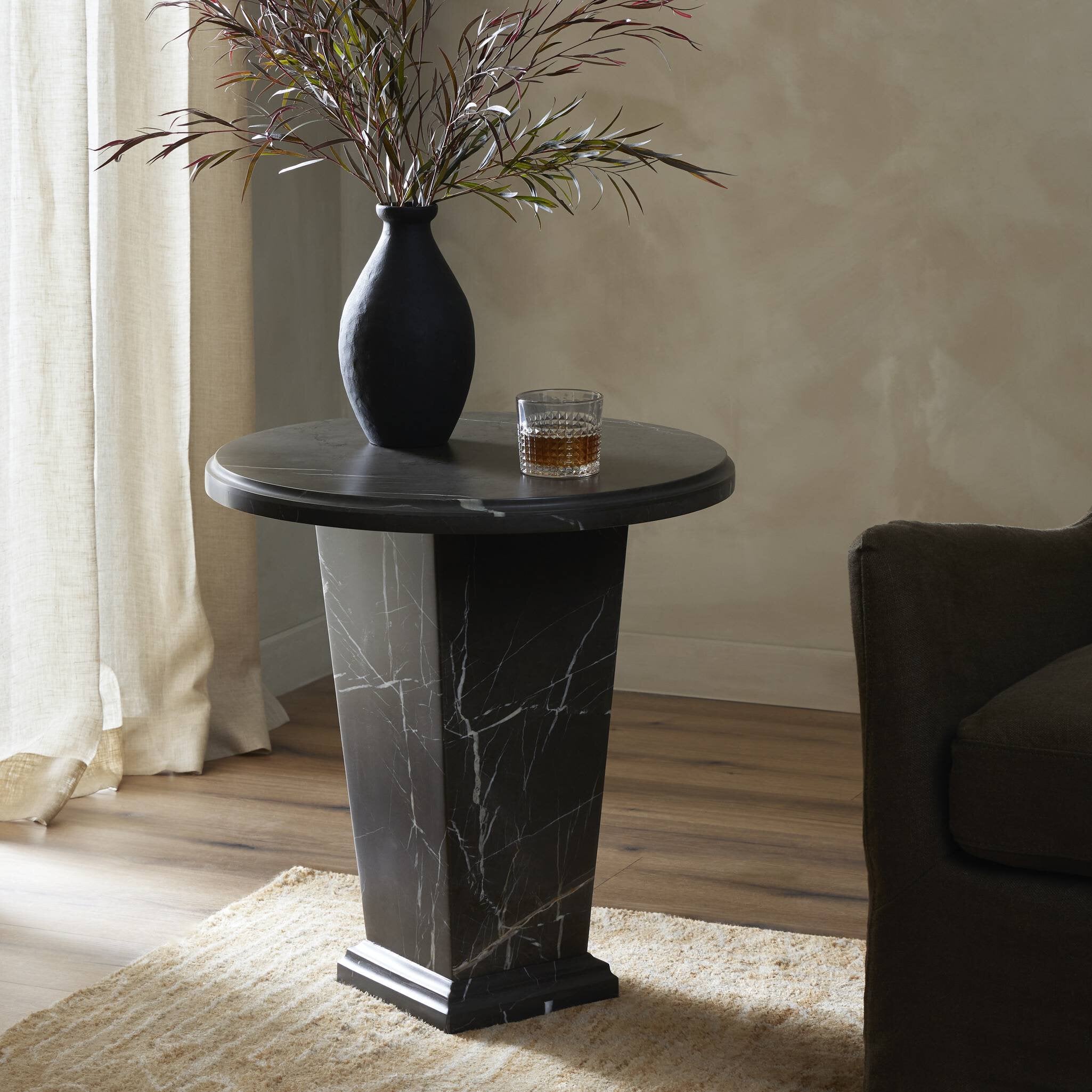 Round dark marble  end table with a vase and glass in a room setting.