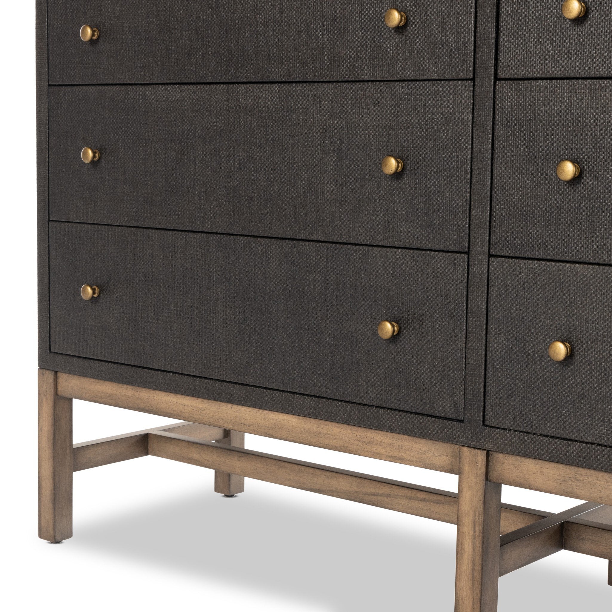 Close up of a black dresser with brass knobs with wooden legs on a white background.
