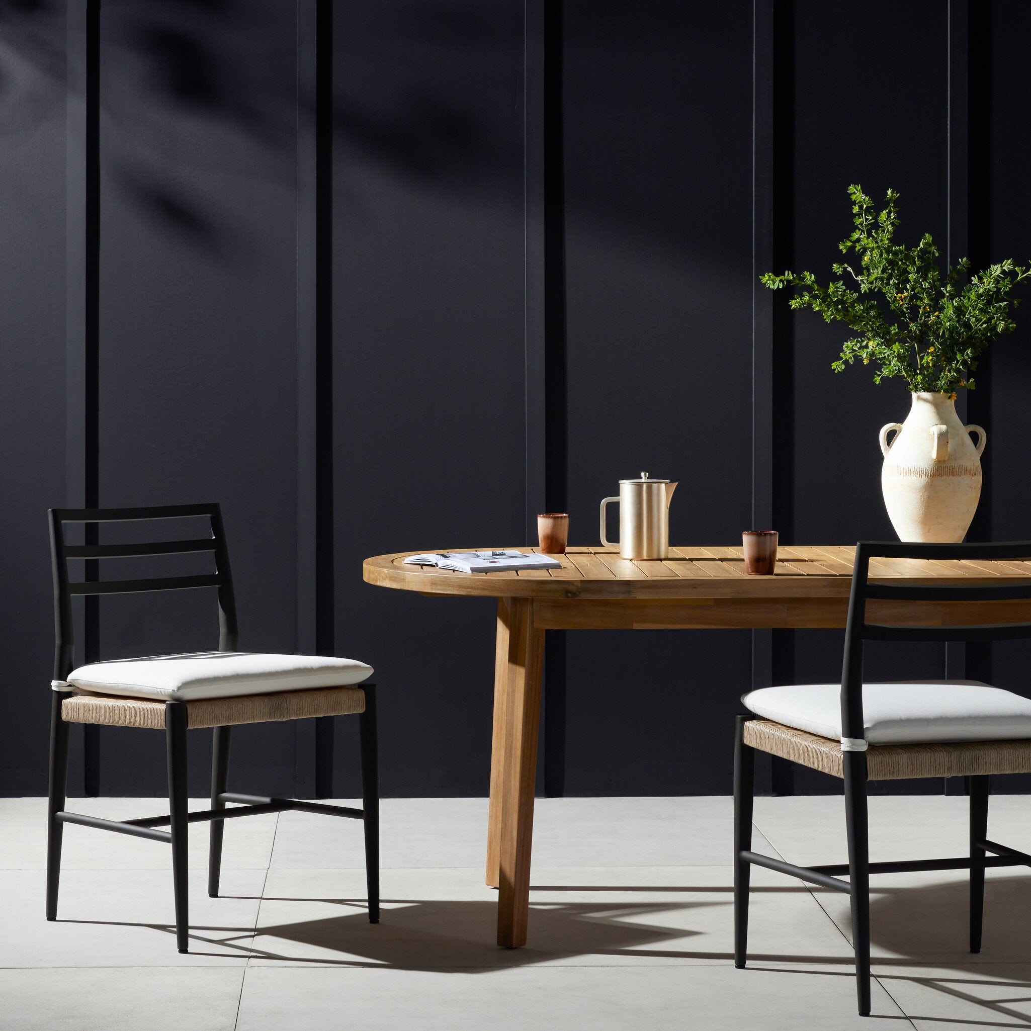 Outdoor dining table with chairs against a dark paneled wall