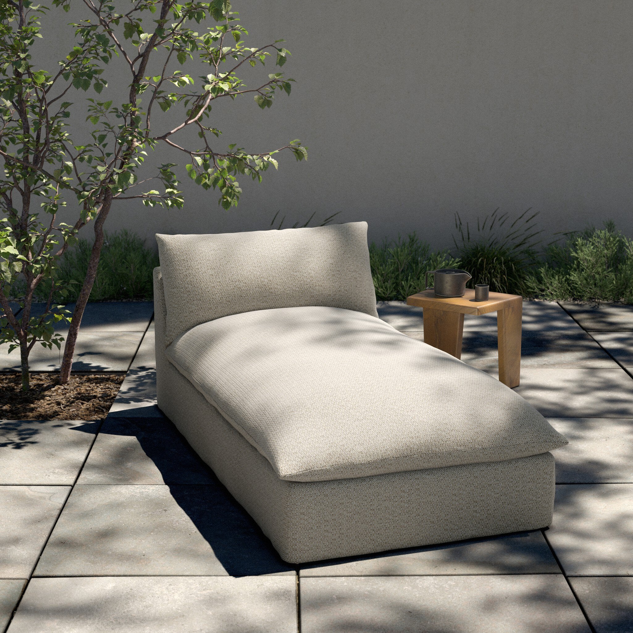Beige outdoor chaise lounge on a patio with plants and a table in the background