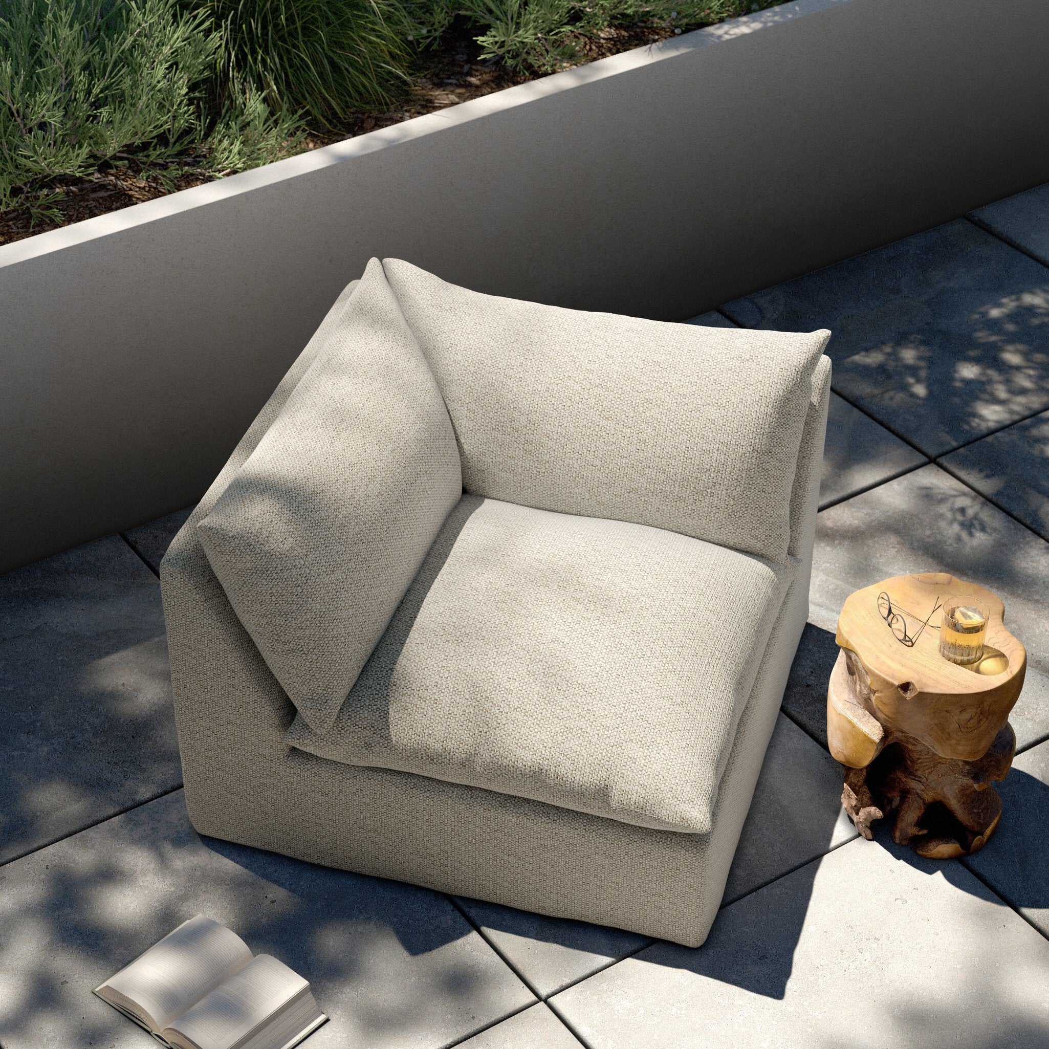 Beige corner section of an outdoor sofa on a patio with a small table and plants in the background.