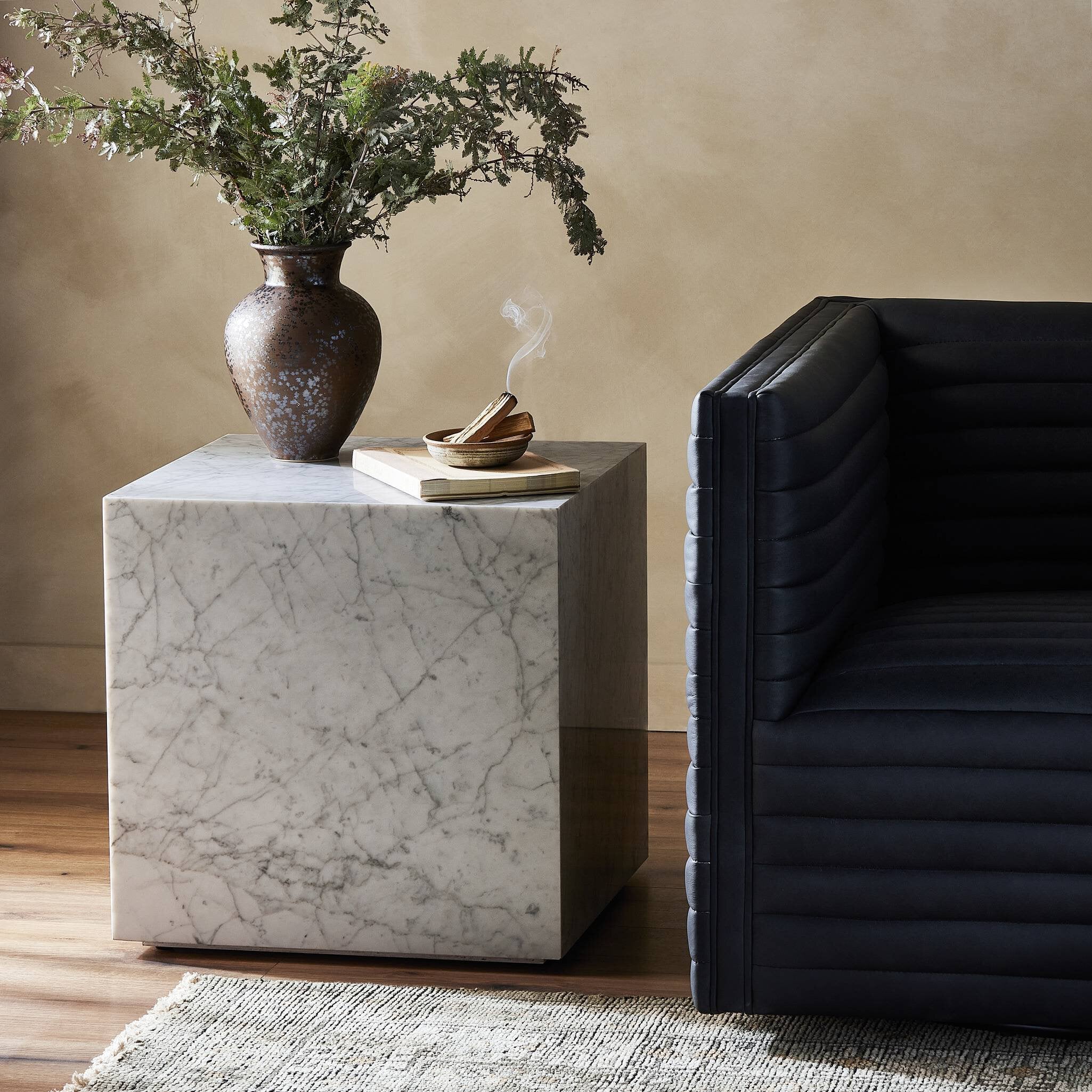 Marble side table with decorative items next to a black sofa.