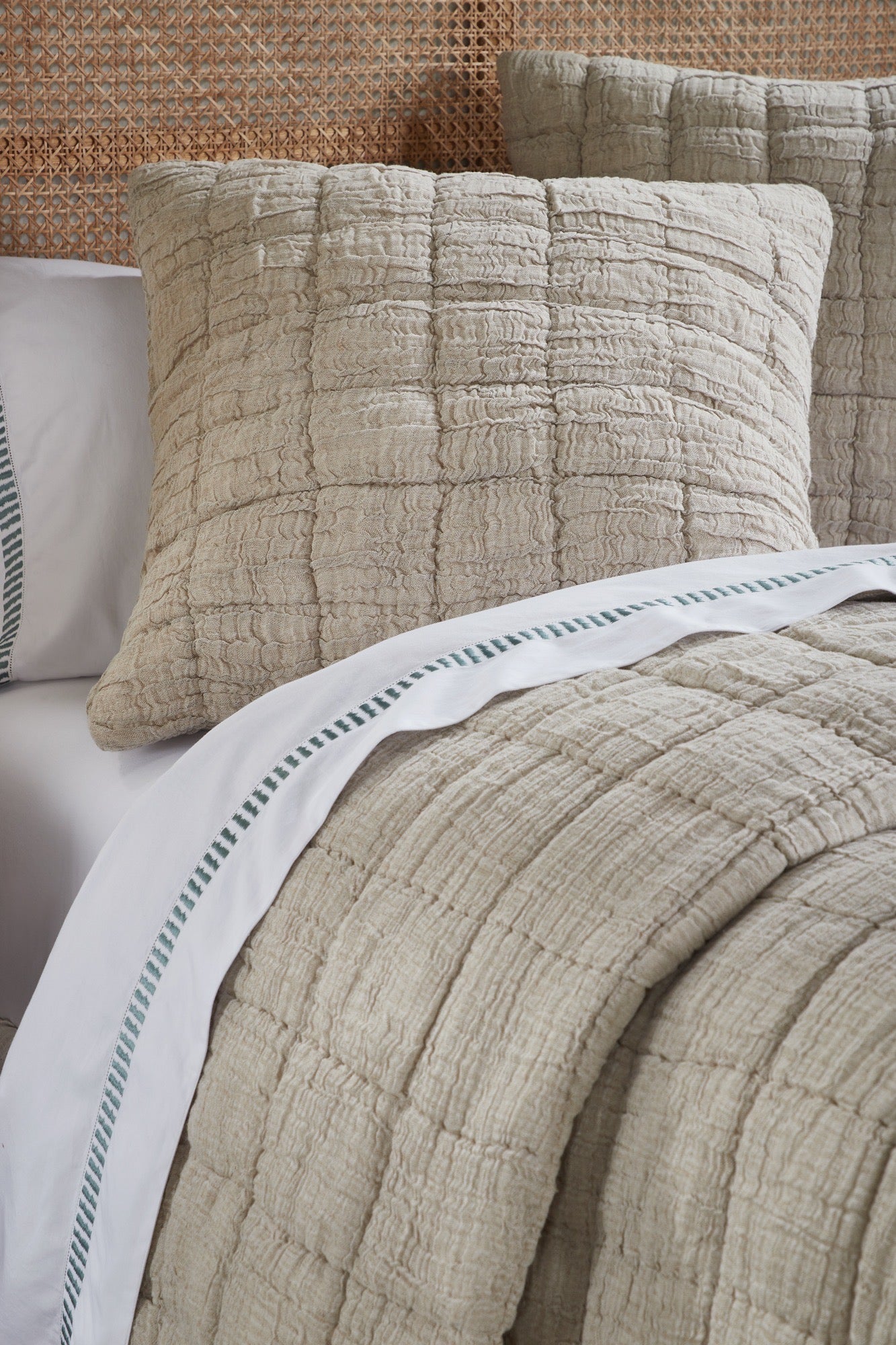 A bed styled with a beige cotton-linen quilt and shams layered atop cream bedding with hand-stitched texture and relaxed elegance.