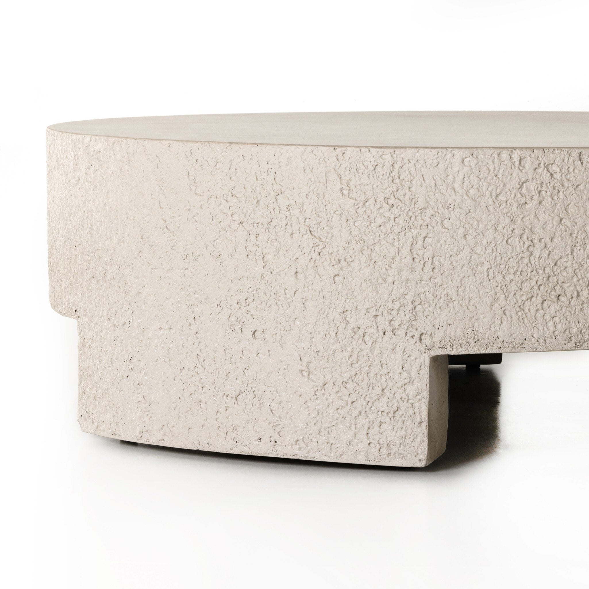 A round pumice concrete coffee table with a smooth top and cutout legs.