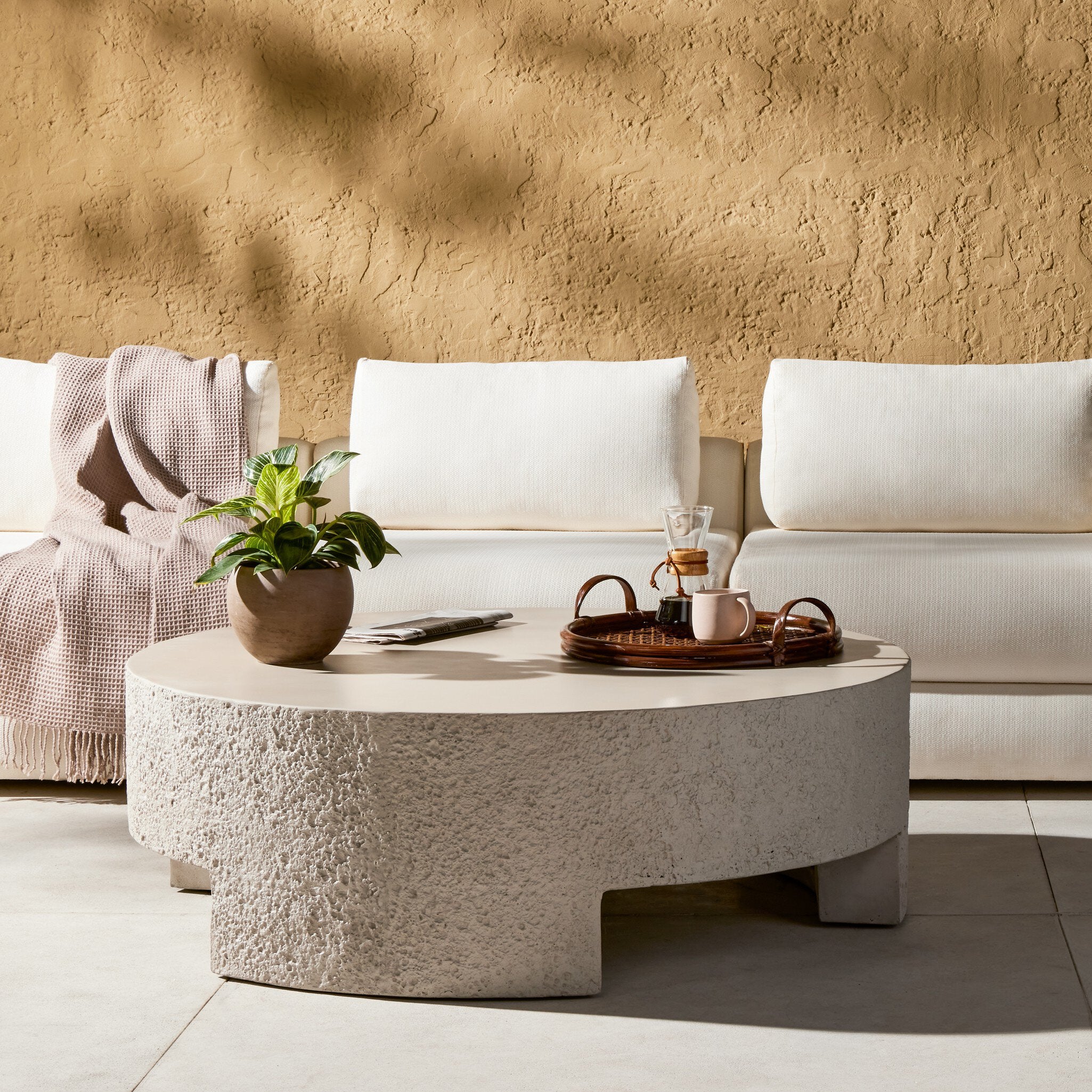 Round concrete coffee table with decorative items in front of a white sofa against a beige wall.