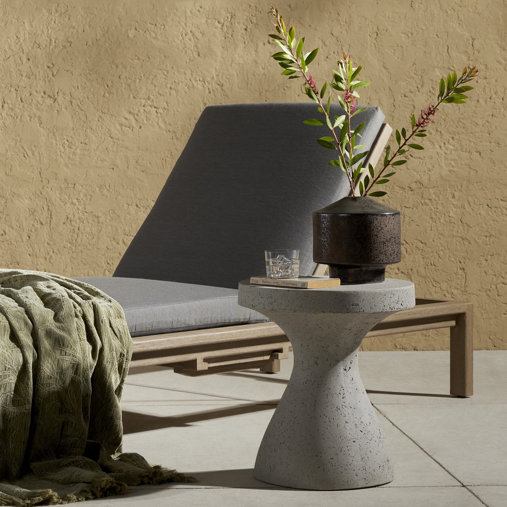 Outdoor setting with a concrete side table, gray lounge chair, and decorative plant.