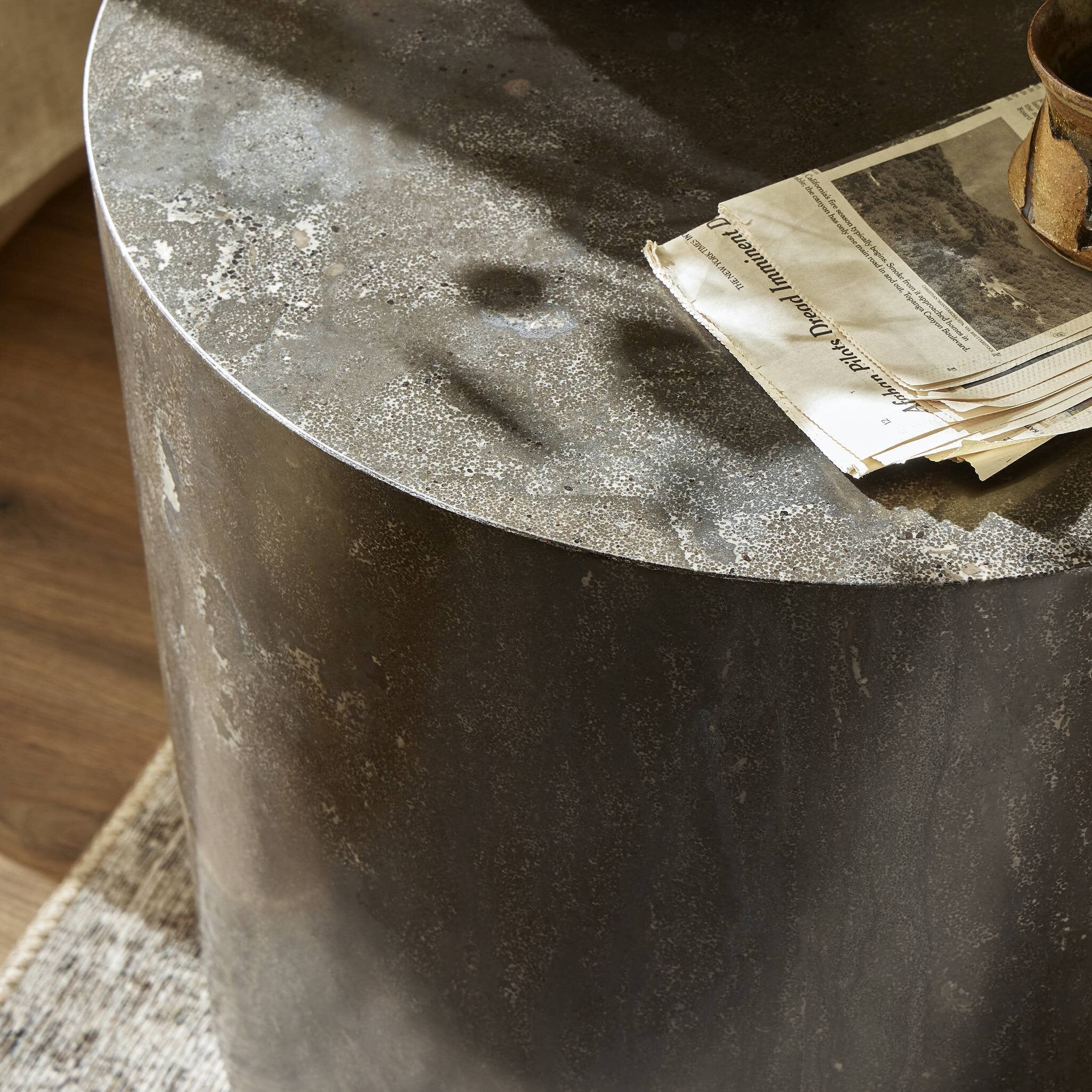 A round stone end table with a textured surface and a newspaper on top.