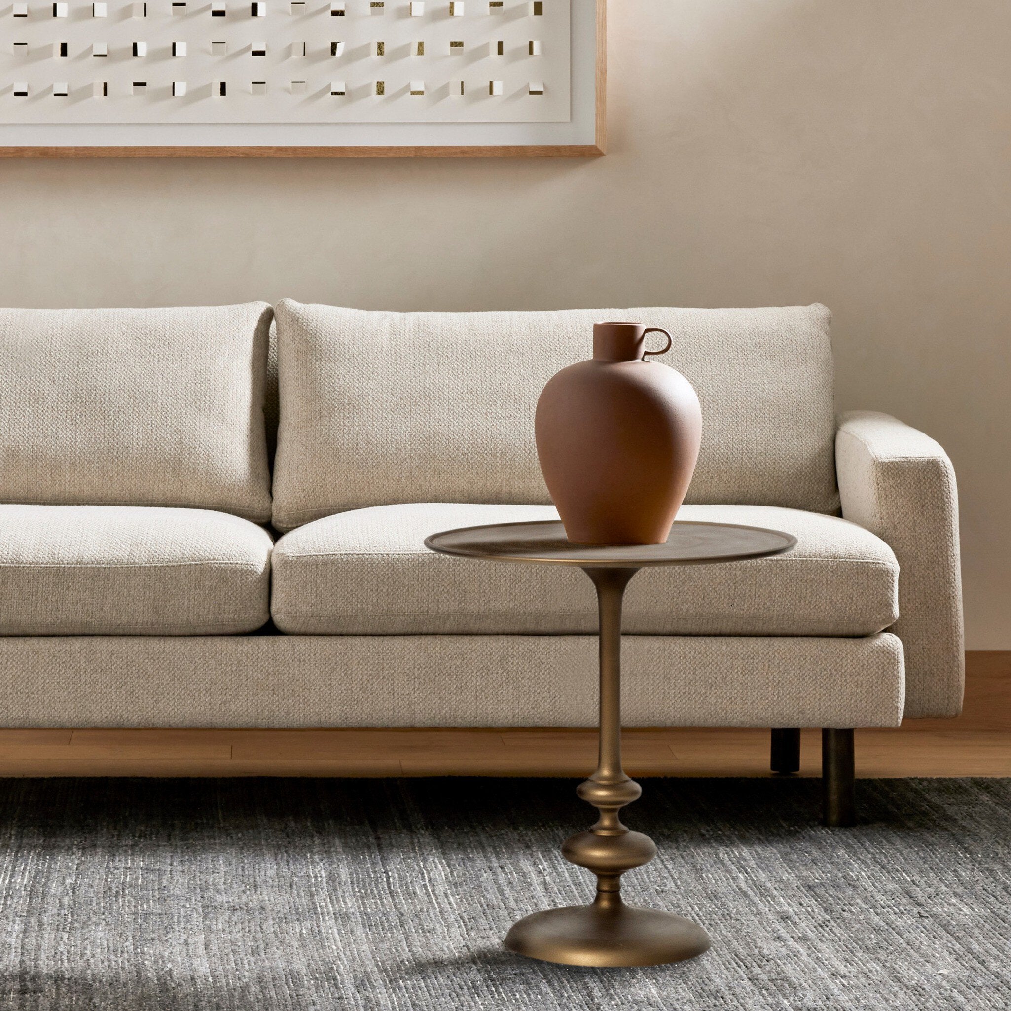 Beige sofa with a bronze side table and decorative vase in a living room setting.