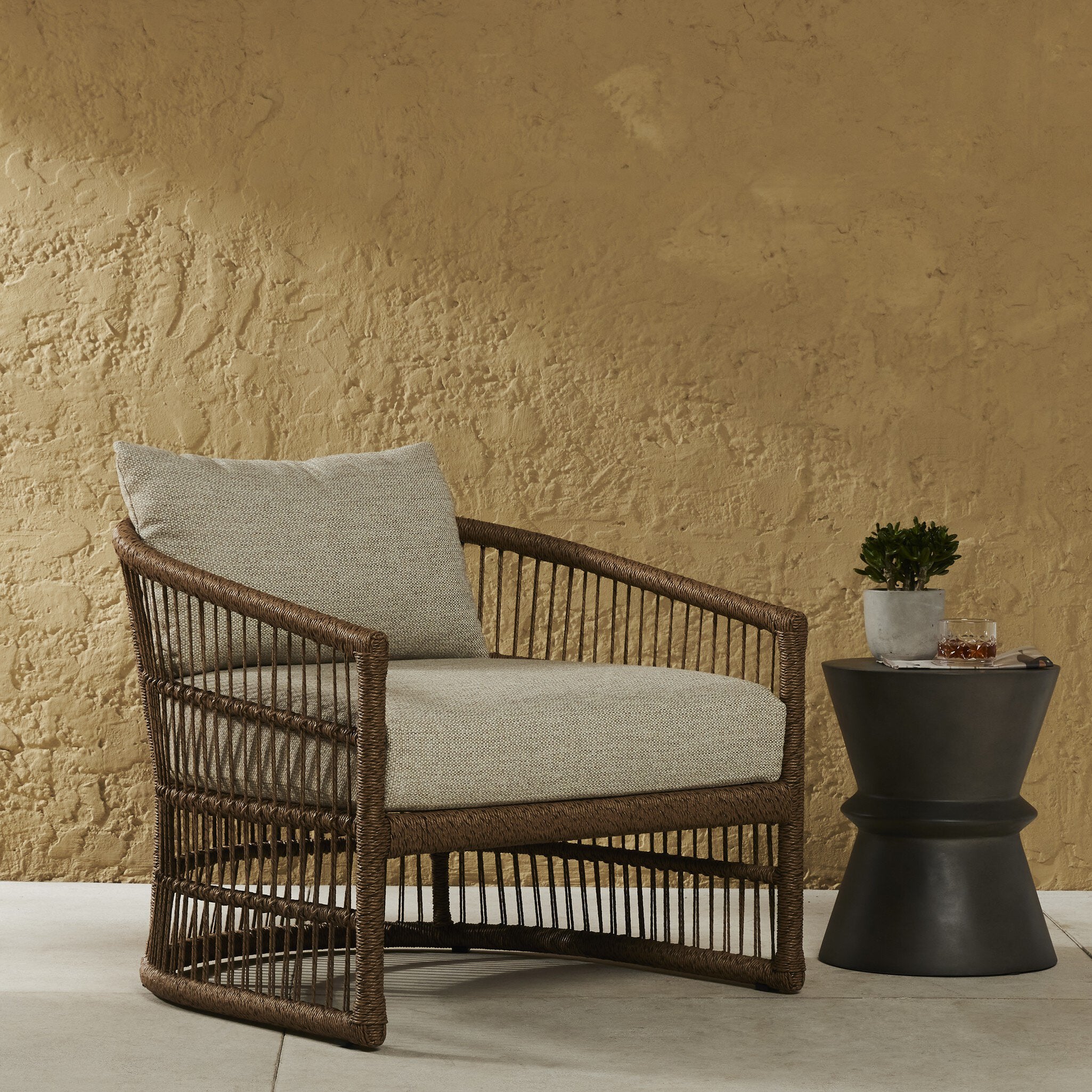 Wicker chair with cushions against a textured beige wall