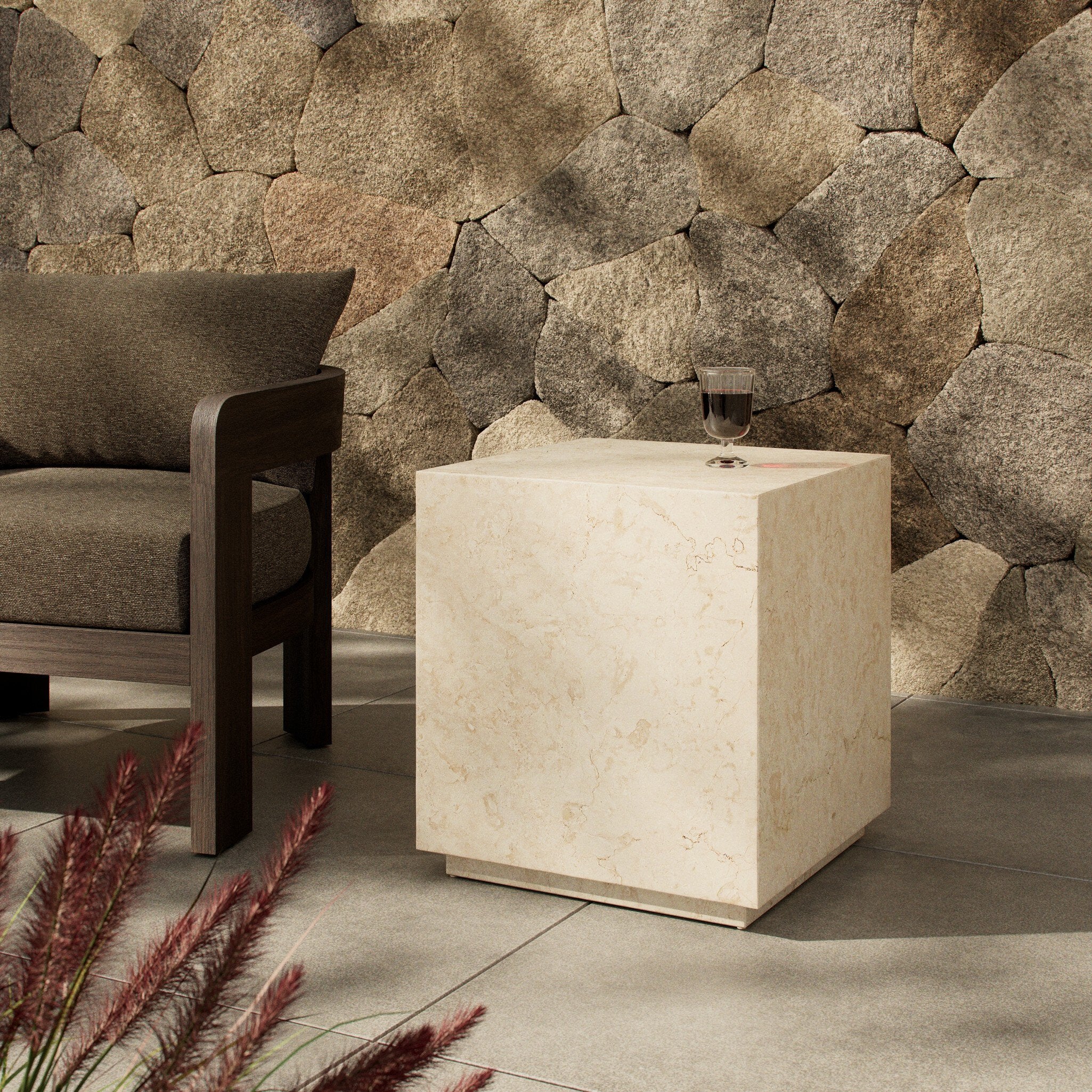 Beige cube-shaped end table against a stone wall with a chair and decorative plants.