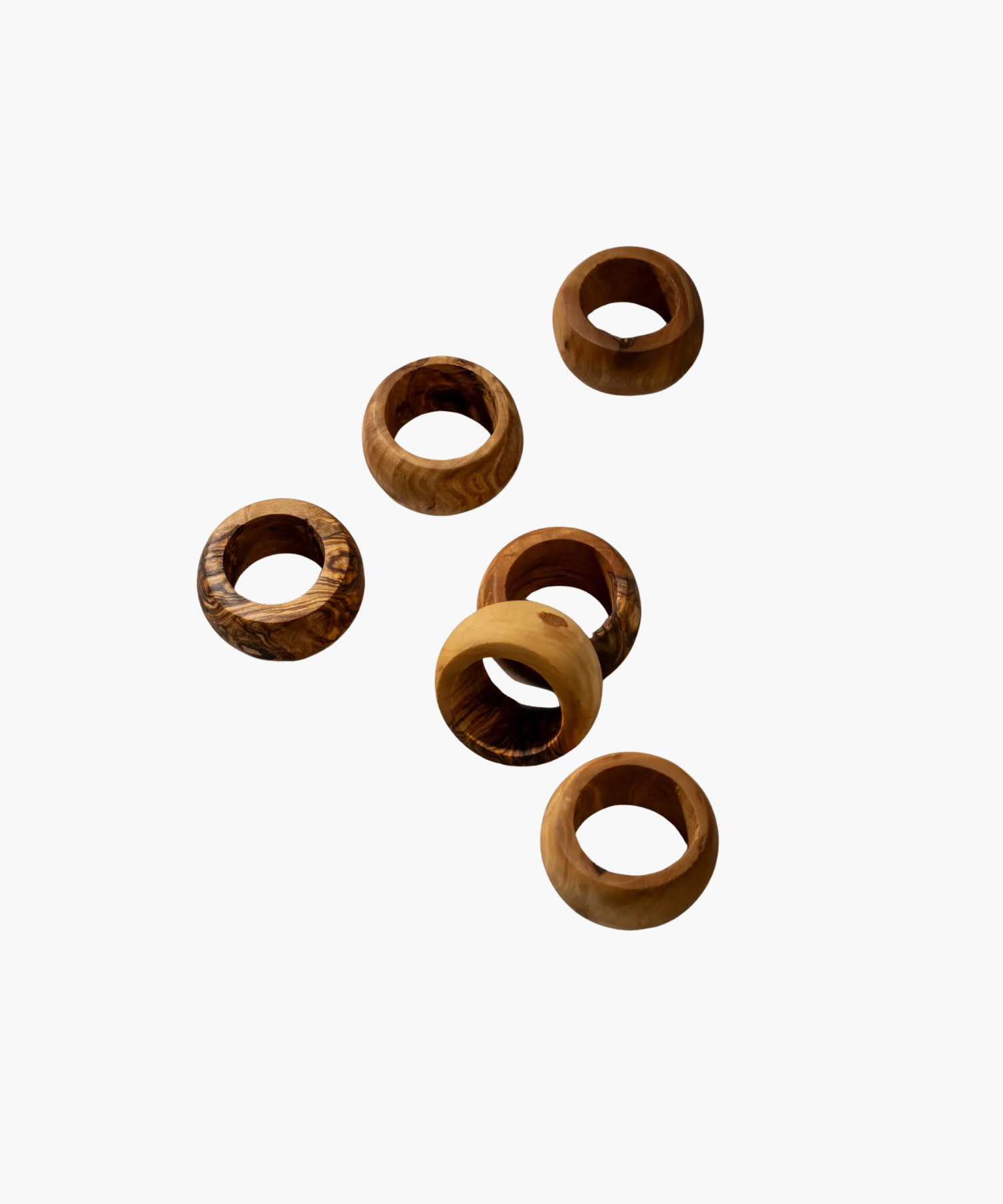 Six wooden napkin rings with varied natural grain patterns are scattered on a plain white background, showcasing a rustic and earthy aesthetic.
