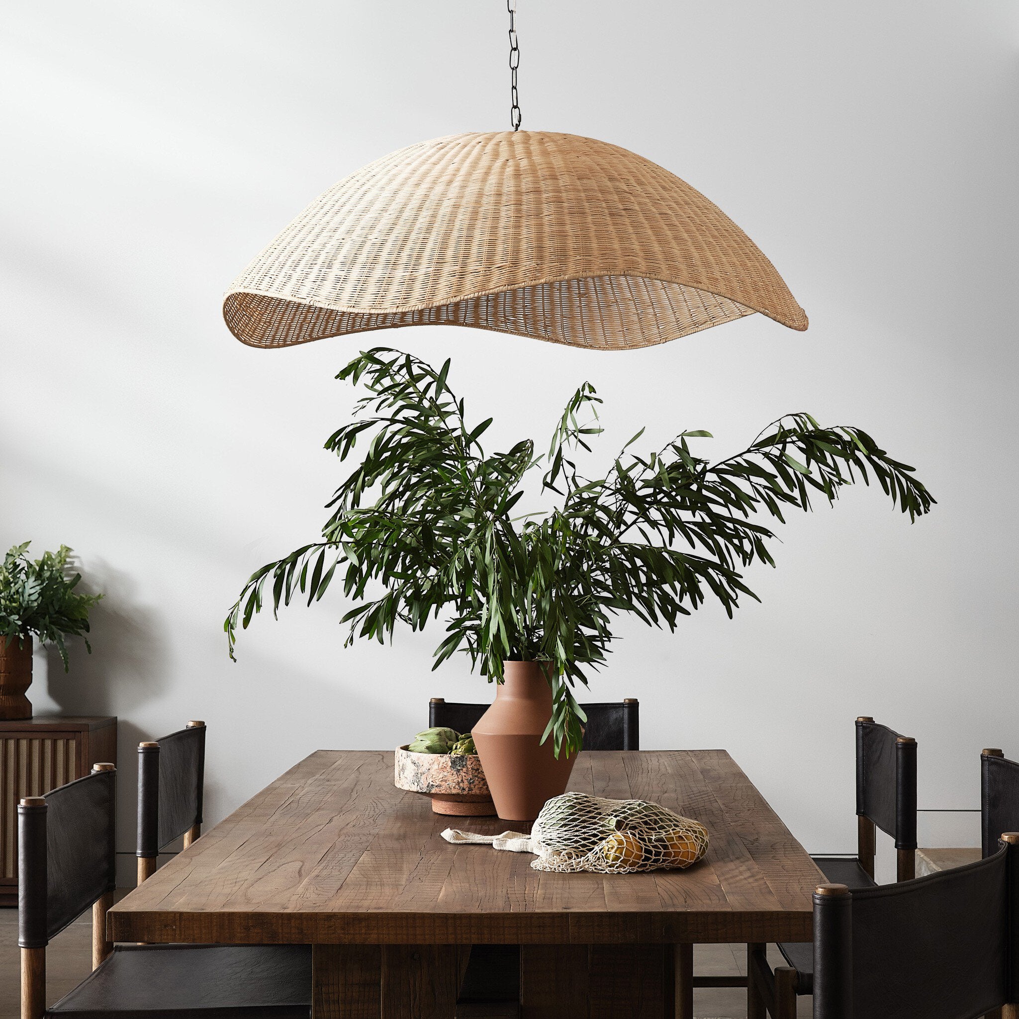 Dining area with a wicker pendant light, wooden table, and potted plants.