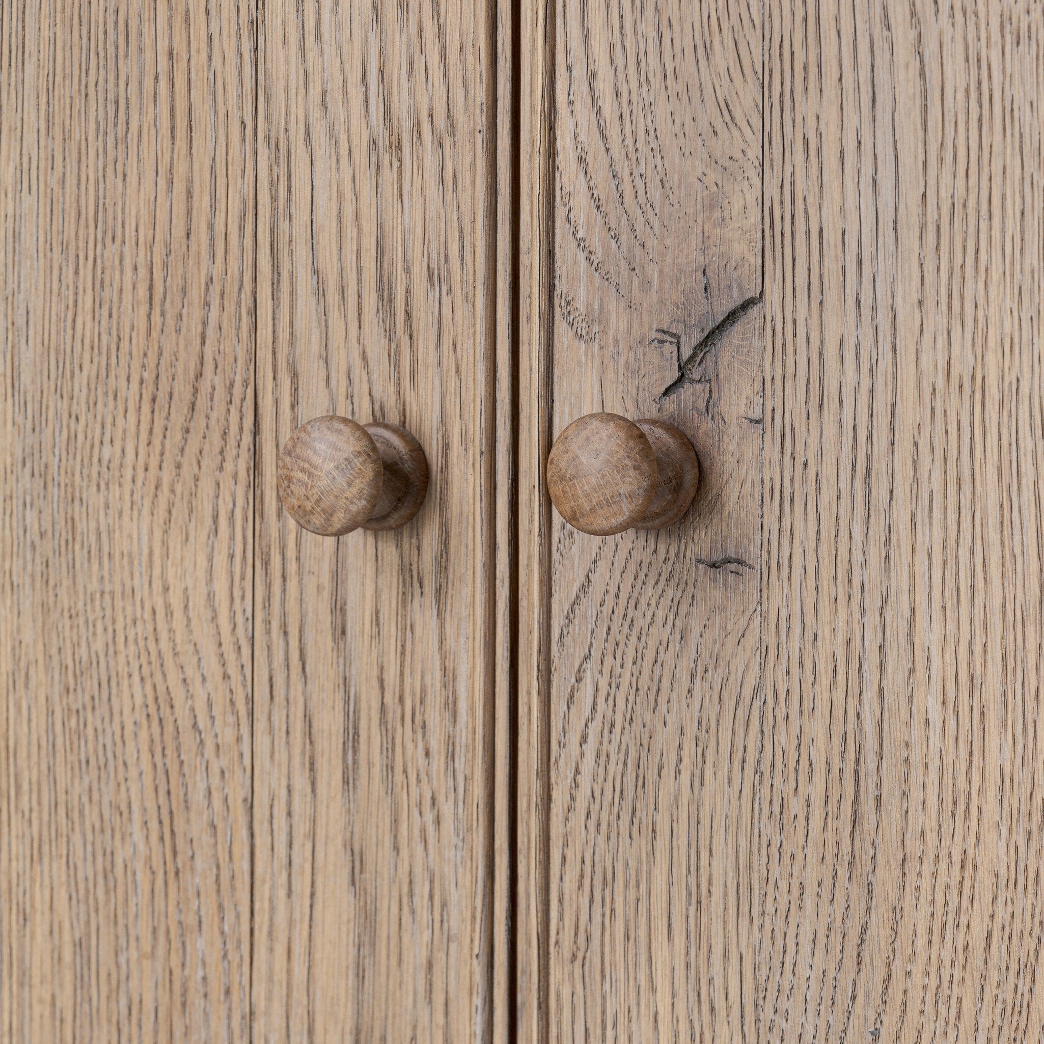 Close-up of wooden armoire doors with round knobs on a light wood background.