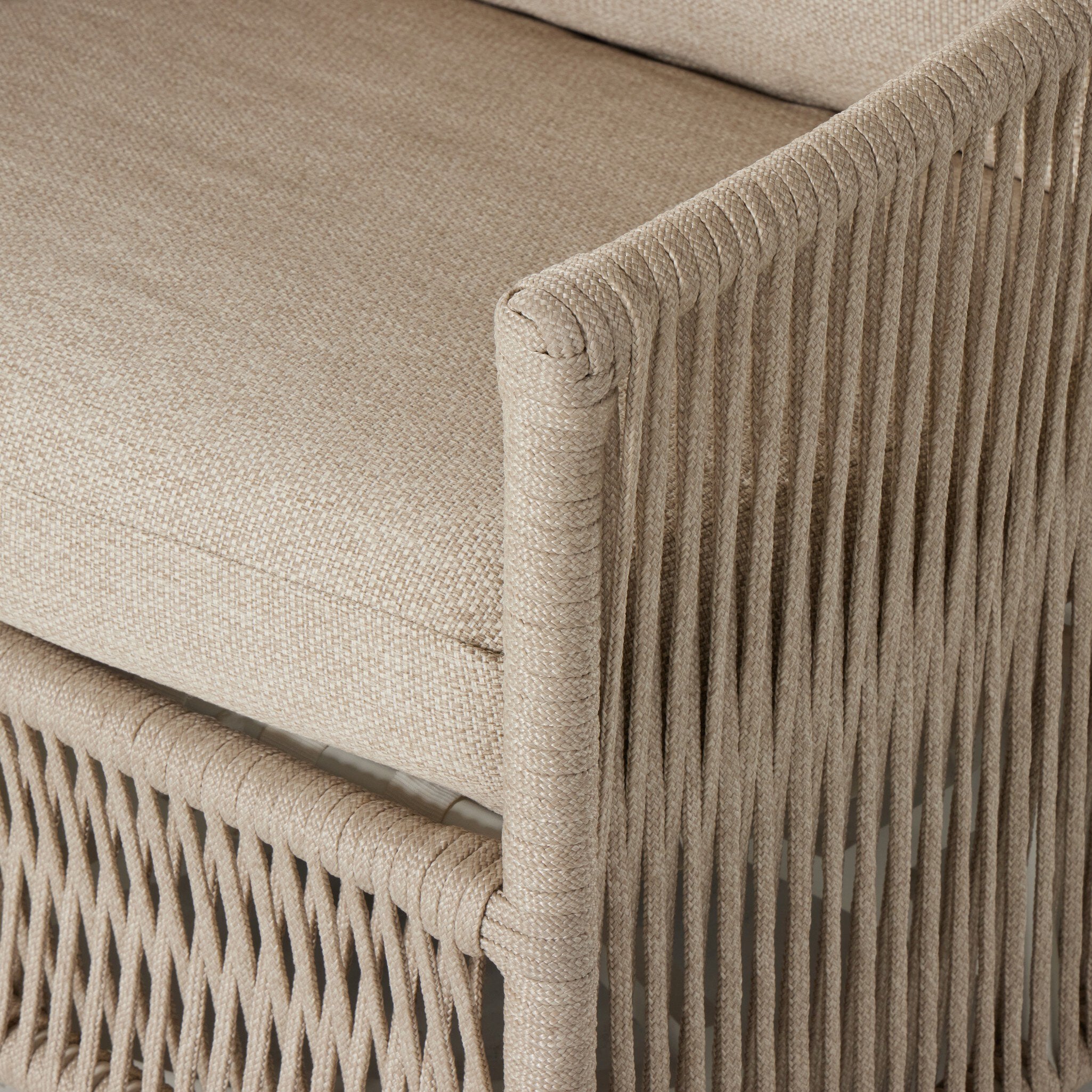 A close up view of a rope based-designed swivel chair in a sand color with a wide cushion and throw pillow on a white background. 
