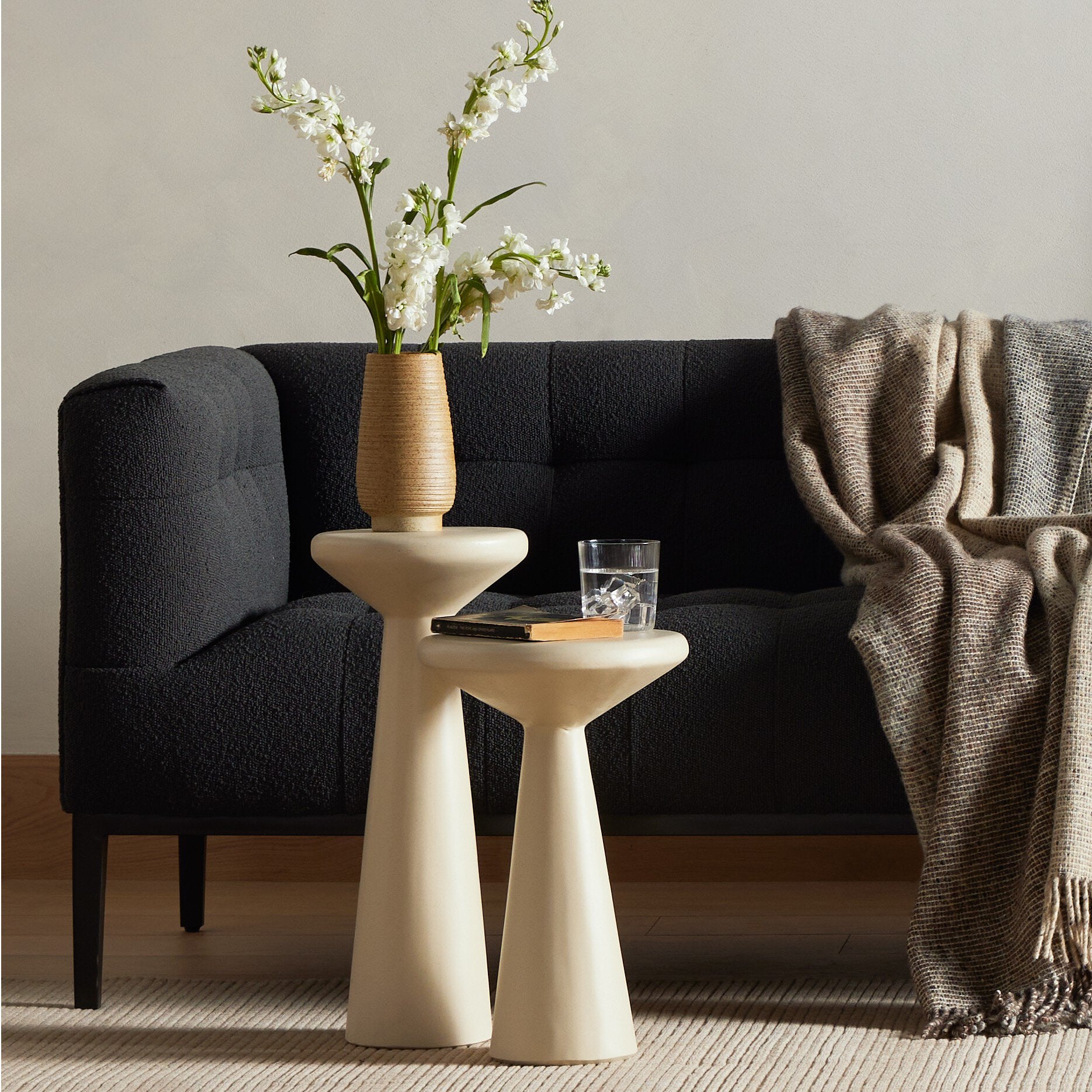 Living room with a dark sofa, white side table, and vase with flowers.