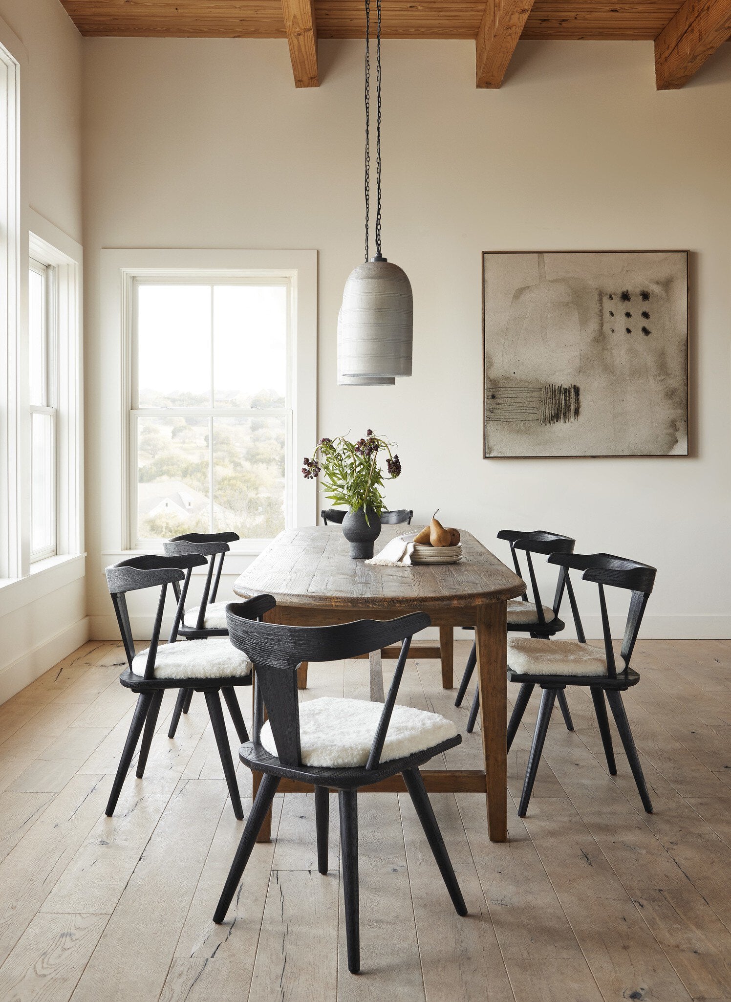 Dining room with wooden table and black chairs, pendant light, and abstract painting.