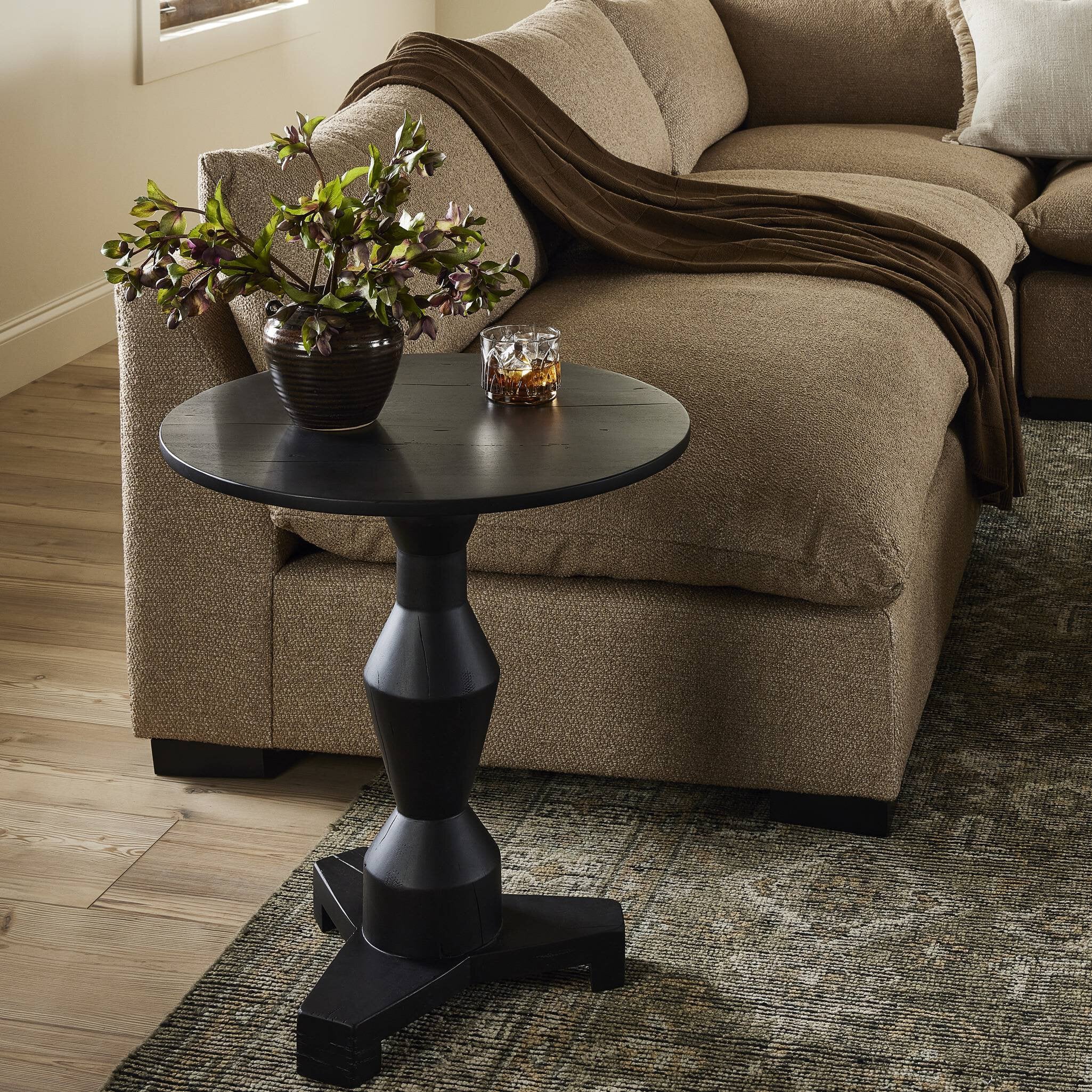 Black side table with a plant and glasses next to a beige sofa in a living room.