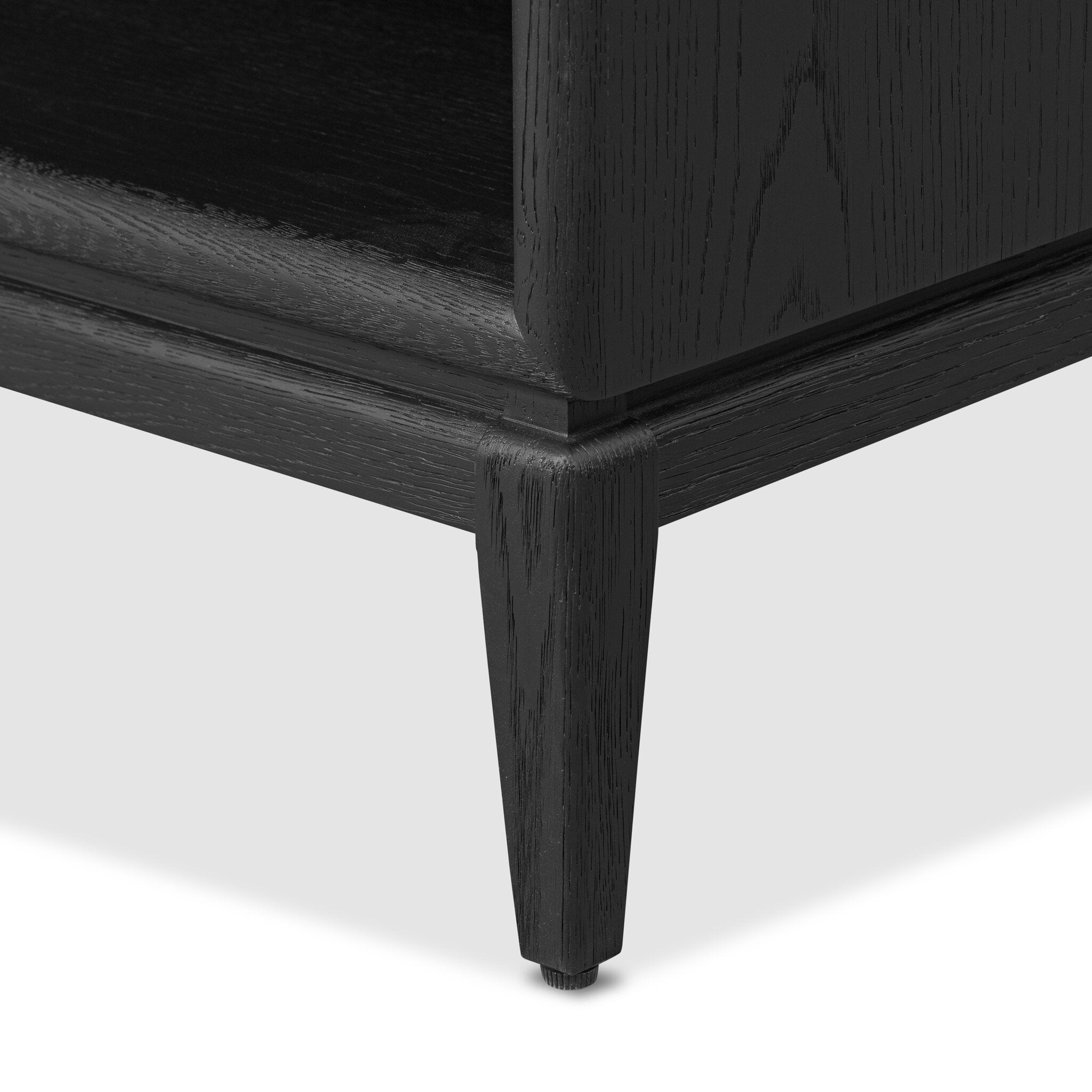 Close up of a black-finished oak nightstand with a smooth top and single drawer front of woven paper on a white background. 