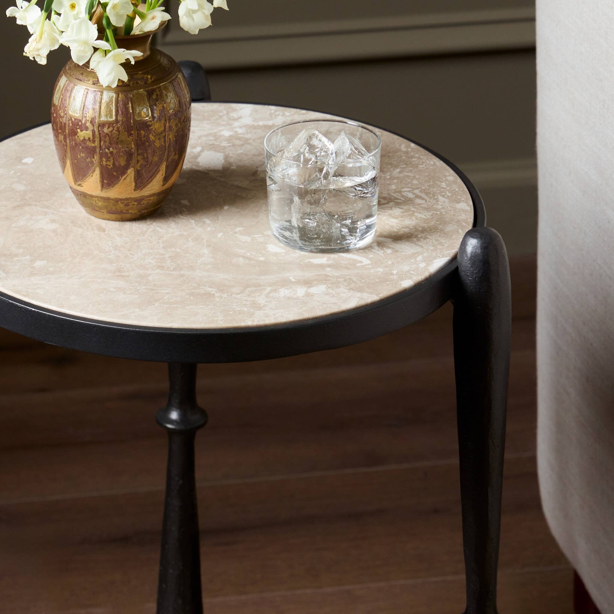 Round marble side table with a vase and glass on a wooden floor.