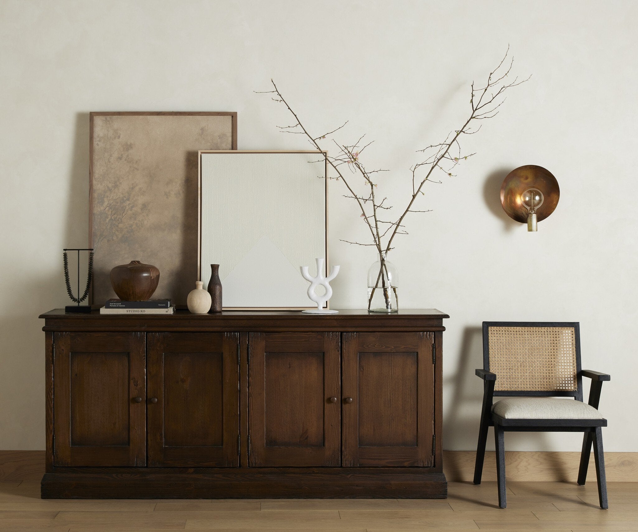 Wooden sideboard with decorative items in a room with a chair and wall sconce.