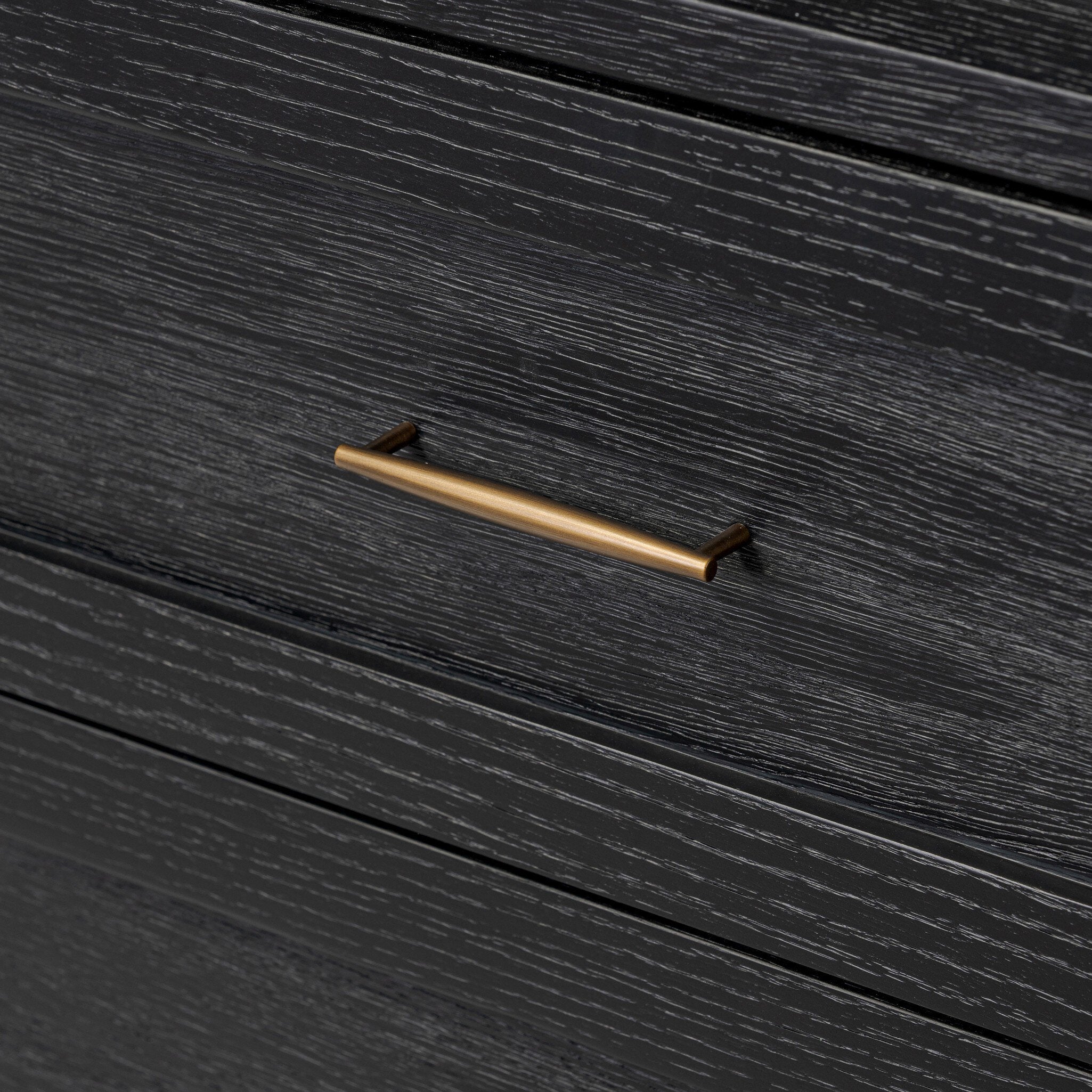 Close up of a curved black dresser with brass handles on a white background.