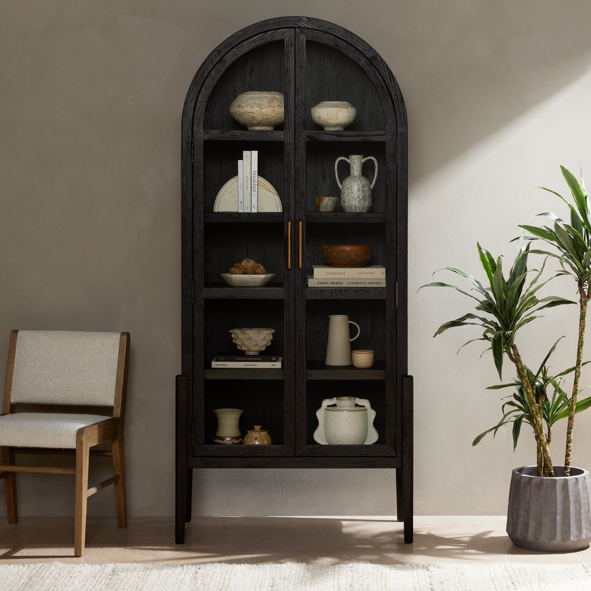 Dark wooden bookshelf with decorative items in a room with a chair and plant.