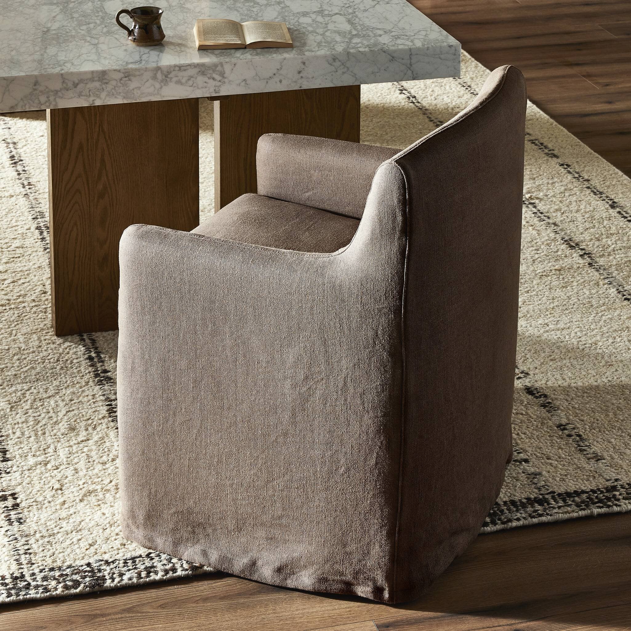 Brown slipcovered dining chair against a marble dining table on a patterned rug.