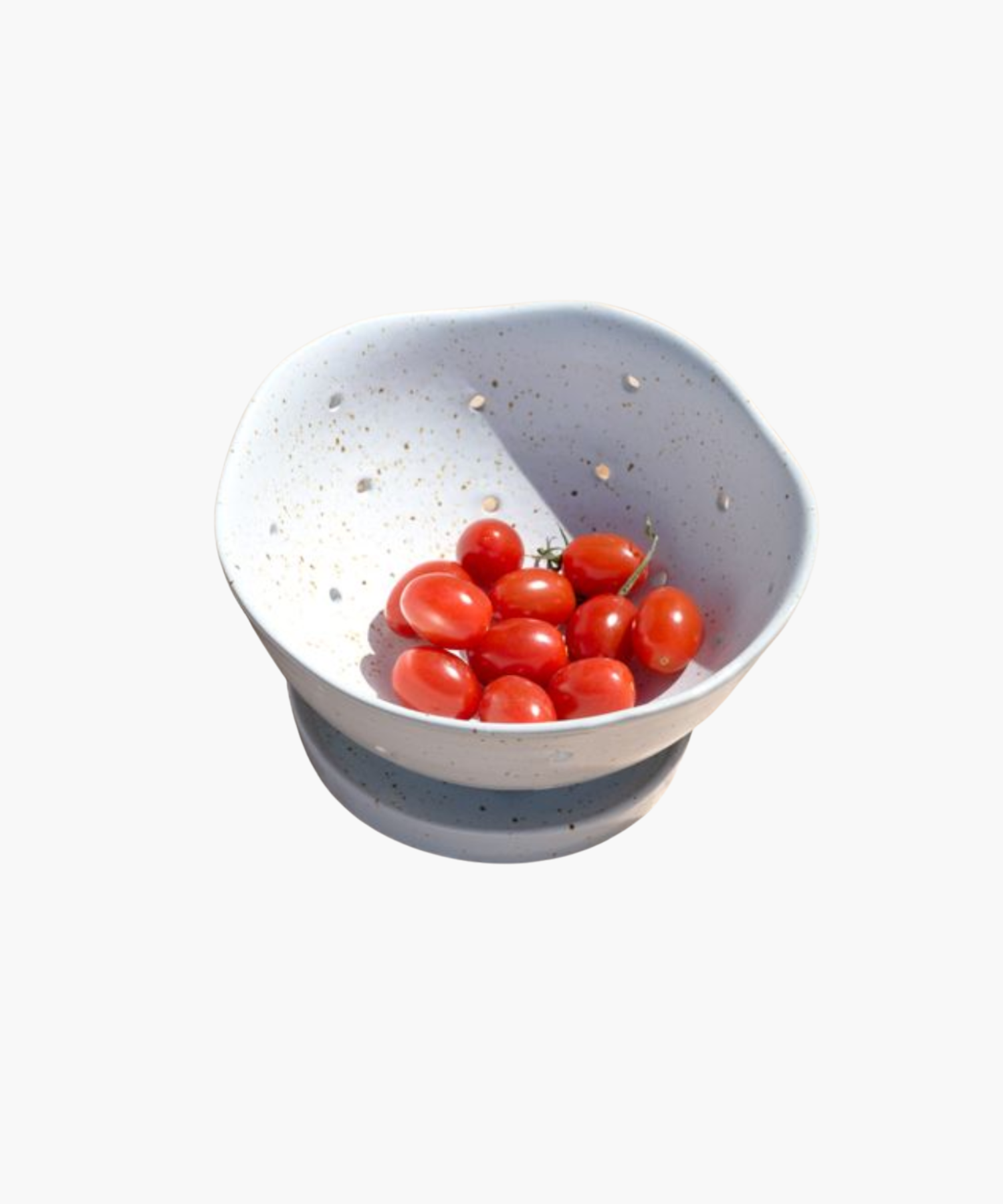 A white speckled ceramic bowl with drainage holes holds several vibrant red cherry tomatoes, creating a fresh and rustic tone.