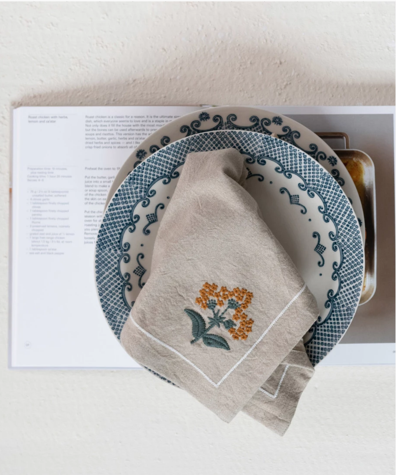 A beige cloth napkin with orange floral embroidery folded open on a plate, suggesting elegance and simplicity.
