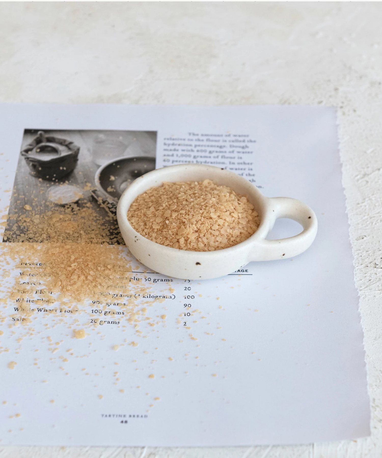 Minimalist ceramic bowl with speckled texture and a round handle on the right side. Its earthy tones convey simplicity and elegance.
